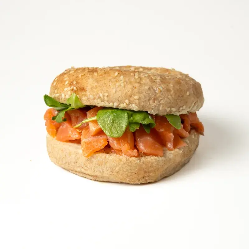 Bagel de sésamo relleno de salmón en dados y hojas verdes