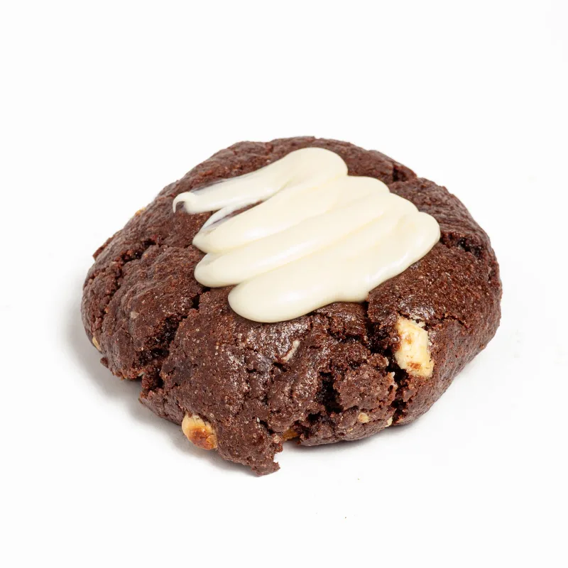 Cookie de masa de cacao con trozos de chocolate blanco y crema blanca por encima, sobre fondo blanco