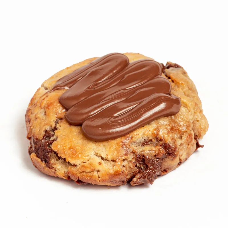 Cookie de masa dorada con pepitas de chocolate y crema de chocolate con leche por encima, sobre fondo blanco