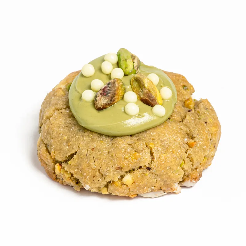 Cookie de pistacho con crema de pistacho, pistachos enteros y bolitas blancas por encima