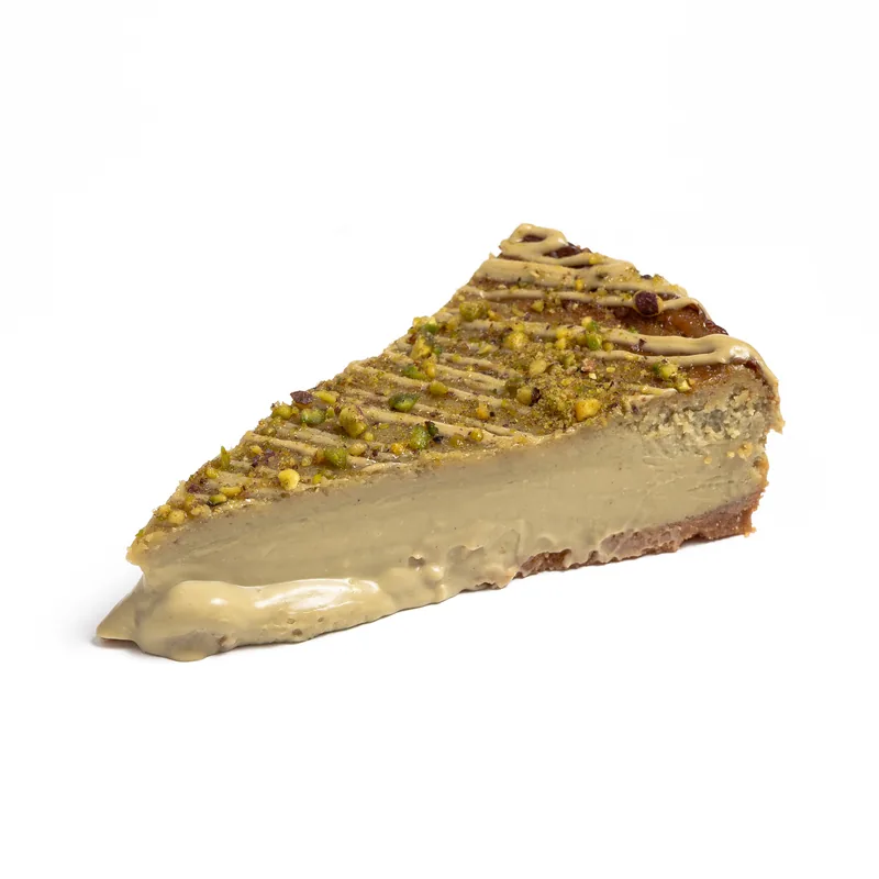 Porción de tarta de queso de pistacho con pistacho picado e hilos de crema de pistacho, de interior cremoso